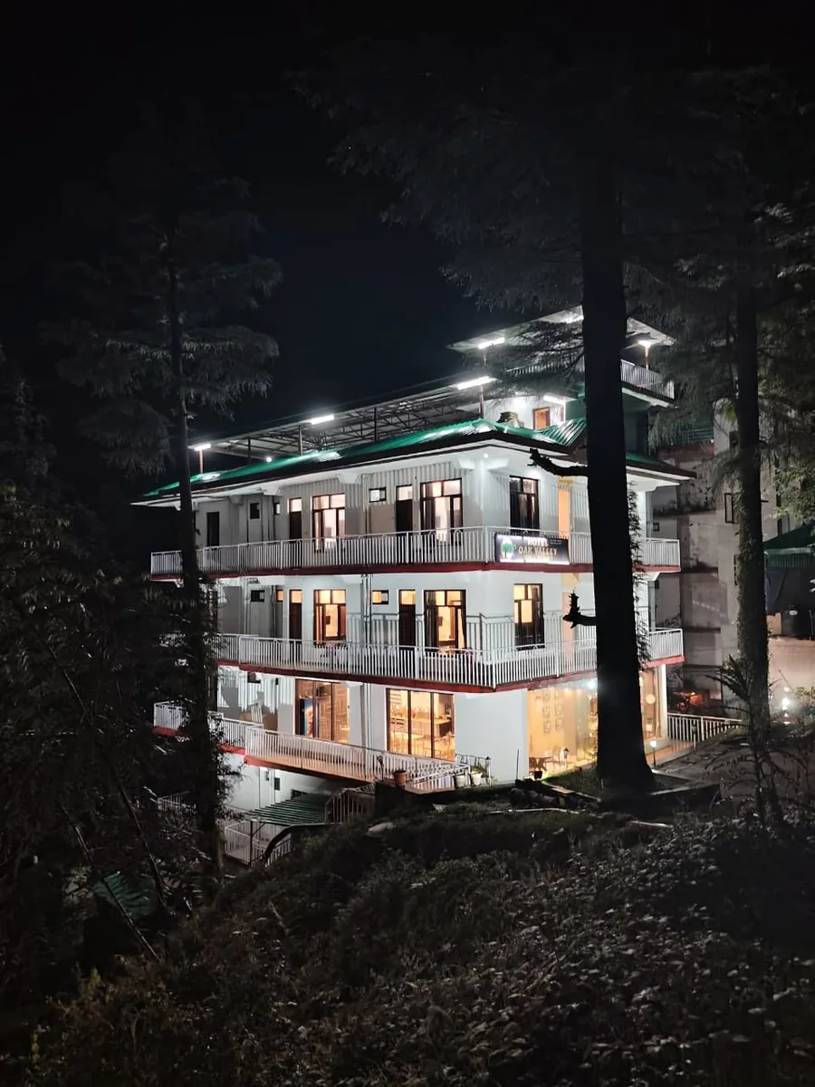 Hotel The Oak Valley lit up at night among the deodars, balconies glowing on every floor